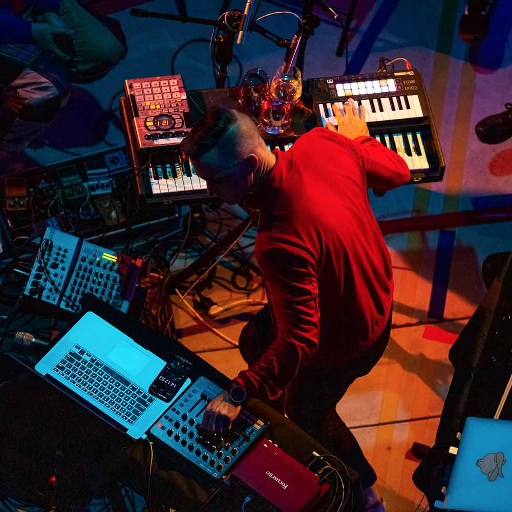 Photograph of Timothy Fairless performing live music. Shot from above, the photograph shows a laptop, a vintage electric piano, sound mixers, and microphones.