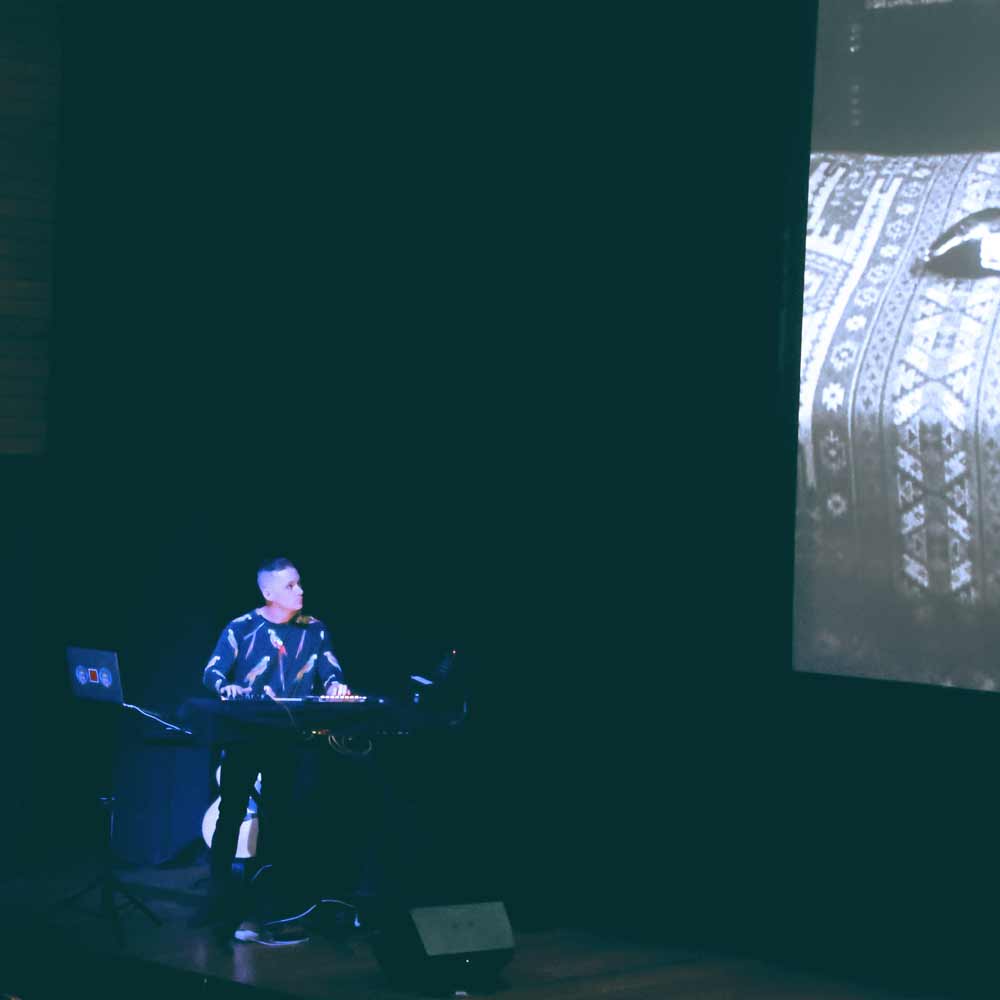 Photograph of Timothy Fairless performing live music. Shot from above, the photograph shows a laptop, a vintage electric piano, sound mixers, and microphones.